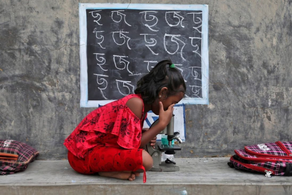 Một bé gái sử dụng kính hiển vi khi tham gia lớp học ngoài trời tại làng Joba Attpara ở bang Tây Bengal, Ấn Độ vào ngày 13.9.2021 - Ảnh: Reuters